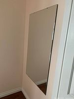 Large rectangular wall mirror hung on a beige wall, showing the frame edges and reflecting part of the room.