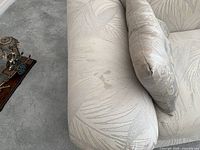 Close-up photo showing minor stain on grey fabric upholstery on armrest of seating piece.