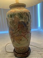 Close-up of a ceramic table lamp showing a raised design of a warrior with horse, detailed with ornate patterns on a wooden base under a fabric lampshade.