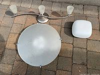 Three overhead lights displayed on ground: curved 3-light fixture, round frosted glass light, square white light.
