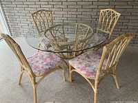Full view of round glass top rattan dining table and four matching chairs with floral cushions
