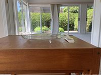 Glass serving dish on wooden surface in front of window, showing its round shape and three small feet.
