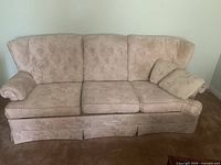 Front view of pink three seat sofa with floral upholstery, cushions, and rolled arms.