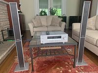 Front view of Yamaha stereo receiver placed on glass table between two Panasonic floor-standing speakers in living room setting.