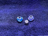 Photo showing three vintage Pandora charms on a blue textured fabric background: two glass bead charms with floral designs and one metal floral charm.