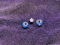 Photo showing all three Pandora charms on a dark textured background: two blue glass bead charms with silver cores and one silver flower charm with a small clear gemstone.