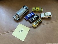 Photo showing six assorted toy cars on a brown surface with a note labeled '3'.