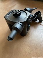 Black battery operated air pump with three plastic nozzle attachments placed on a tan surface.