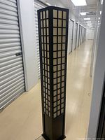 Full view of the tall rectangular Asian style floor lamp with black wood frame and grid-like translucent panels.