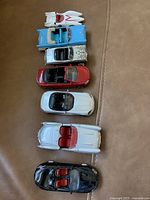 Seven assorted convertible toy cars arranged on a brown surface, showing the top and side views