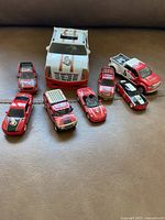 Nine assorted toy cars and one toy truck in red, black, and white colors arranged on a surface.