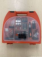 Closed orange plastic tool box with clear lid showing multiple compartments filled with drill bits and screwdriver bits, bearing Black & Decker logo.