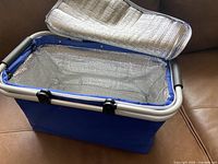 Blue soft sided cooler bag open showing silver reflective insulated inner lining and zippered lid.