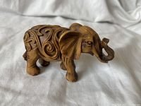 Overall view of carved wooden elephant figurine showing detailed swirl carvings, raised trunk, and polished wood texture.
