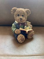 Front view of ceramic teddy bear figurine sitting and reading a book, holding a smaller teddy bear.