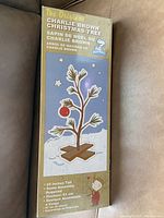 Photo of the box front showing the original Charlie Brown Christmas Tree with text indicating height and assembly requirement