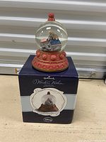 Water globe showing a mother elephant and baby inside, sitting on a decorative red and gold base. Globe is placed on its original box showing Hallmark and Disney branding.