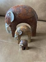 Photo of a set of three elephant figurines in different sizes with carved intricate patterns and silver-colored ears and tusks placed on a couch.