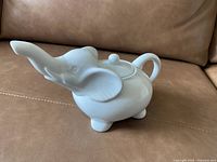 White ceramic tea pot shaped like an elephant placed on a brown leather surface.