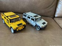Photo showing two Hummer model cars, one yellow and one white, placed on a brown leather surface.