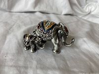 Photo of adult and baby jeweled pewter elephant figurines together on a white fabric background.