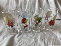 Front view of all four vintage Looney Tunes glasses lined up on a white cloth, showing colorful character prints