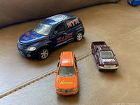 Image showing three toy cars: blue New York Rangers SUV, orange Reese's truck, and maroon Hershey's car, placed on a beige surface.