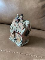 Porcelain figurine of snow-covered two-story brick house with two figures on roof in winter clothes