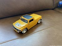 Yellow Hummer toy car model placed on a brown leather surface, showing front and side details, including chrome grille and wheels, black roof panel.