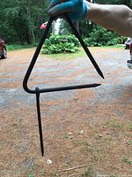 Photo of black metal dinner bell triangle hanging, held by person wearing blue glove. Shows shape and size.