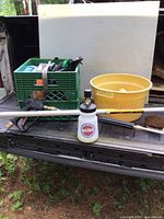 Photo showing green crate with various spray bottles, McKillins foam cannon and stubby sprayer handle, long metal extension pole, yellow plastic tub, and cleaning brushes placed on truck bed.