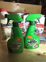 Two green spray bottles of Schultz Indoor Insecticidal Soap with white and red bottle of Roundup in the background.