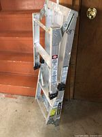 Folded aluminum platform ladder leaning against a wall, showing the general structure and the folded form.