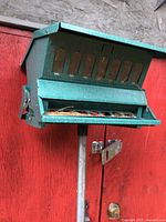 Close-up of green squirrel proof bird feeder mounted on pole with multiple feeding ports and housing design