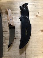 Fixed blade garden cutter knife with wooden handle and black leather sheath on wooden surface.