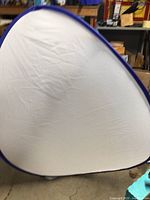 Triangular-shaped portable fabric shelter with white walls and blue trim, standing upright, showing front panel.