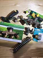 Full lot view showing multiple brass manifold valves by Lee Valley and Orbit, brass hose connectors, a metal spring hose protector, and yellow/green plastic hose connectors.