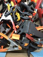 Close-up photo of assorted spring and hand clamps with plastic jaws and handles in orange, black, and yellow colors piled together.