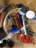 Top-down photo of assorted plumbing tools and fittings spread on a wooden surface with copper pipes, tubing, showerhead, faucet handle, and tape visible.