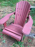 Red wooden Muskoka chair on ground with visible wear and paint chipping