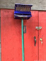 Blue squirrel proof bird feeder mounted on green pole against red wooden background.