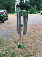 Large silver metal wind chime outdoors, hanging with green clapper visible