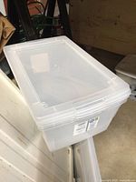 Plastic storage tote with white lid turned upside down showing slight wear on surface.