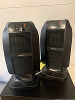 Pair of black Honeywell ceramic space heaters standing side by side on a dark surface, showing full front and base design.