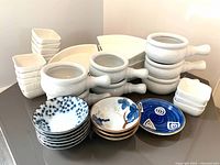 Overview of assorted serveware including stacked white onion soup bowls with handles, modular serving dishes, and various patterned Asian-style bowls.