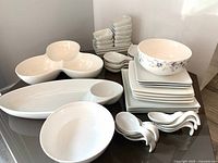 Full view of assorted white ceramic serveware on table including bowls, plates, and tasting spoons