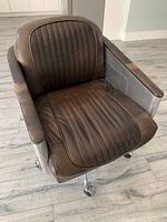 Front angle showing distressed leather seat, channel tufting and padded armrests