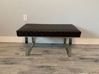 Front view of bench showing woven seat and metal legs.