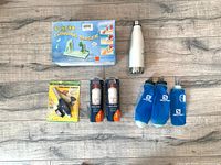 Top-down view of all items including turning slicer in box, white insulated water bottle, handheld torch, two Everydrop filter packages, and three blue Hydrapak bottles arranged on wood floor.