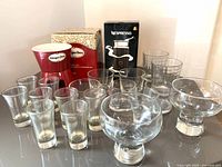Full view of all items included in the lot: Nespresso Aeroccino 3 milk frother box, Häagen-Dazs fondue set, multiple clear glasses of varying sizes including ice cream cups